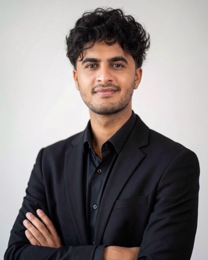 Ketuman in a black jacket and shirt, arms crossed, smiling at the camera